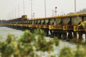 Composição MRS com vagões de minério de ferro atravessando uma ponte sobre espelho d´água